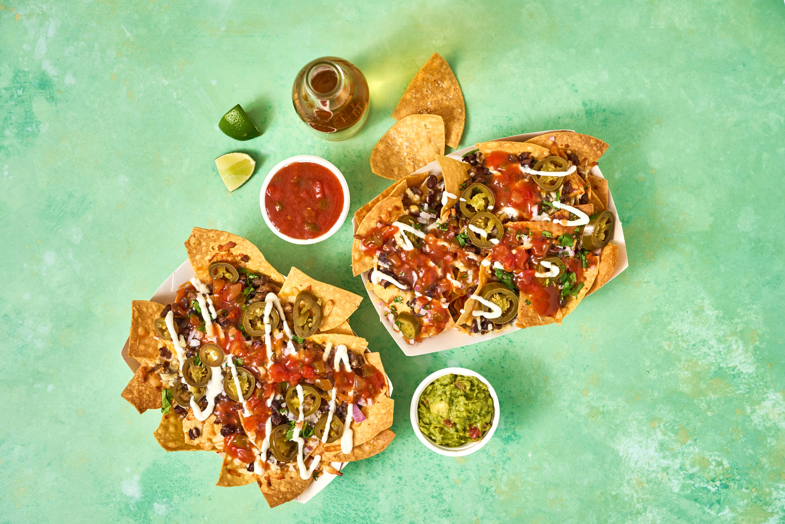 Top down shot of Embasa Salsa Roja Nachos. Salsa, guacamole, lime, and a drink on the side.